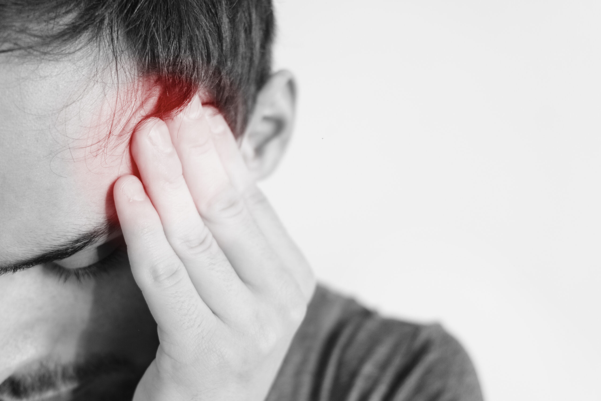 Black and white image of a man holding his head in pain with red pain spot highlighting injury location
